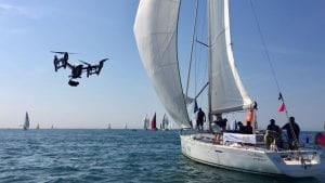 A drone with a camera flies next to a sailing yacht
